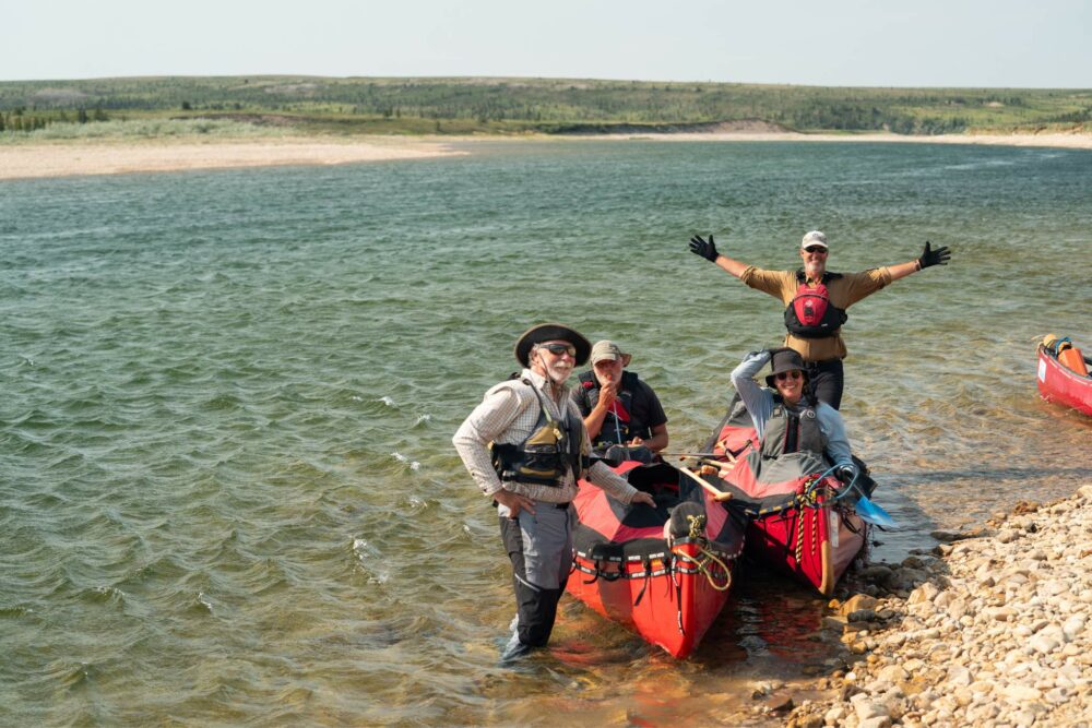 Happy guests posing in canoes on the banks of the Horton River during their expedition.