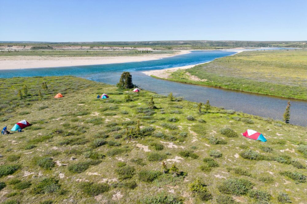A group of people camped next to the Horton River, as viewed from above by a drone.