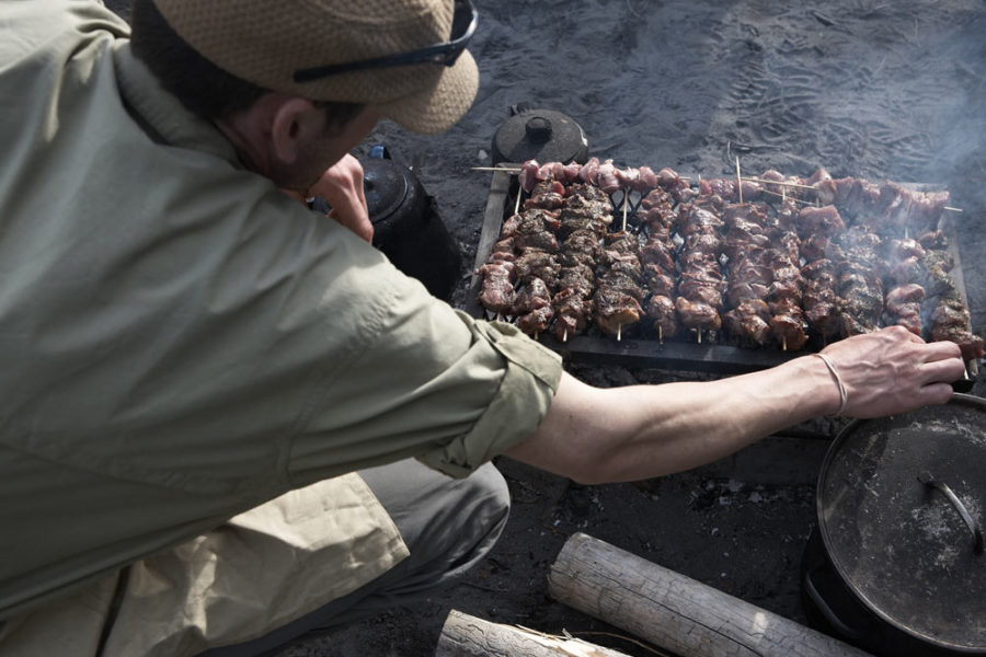 A guide grills some kebabs over an open fire on the shores of the Nahanni River in Nahanni National Park Preserve.