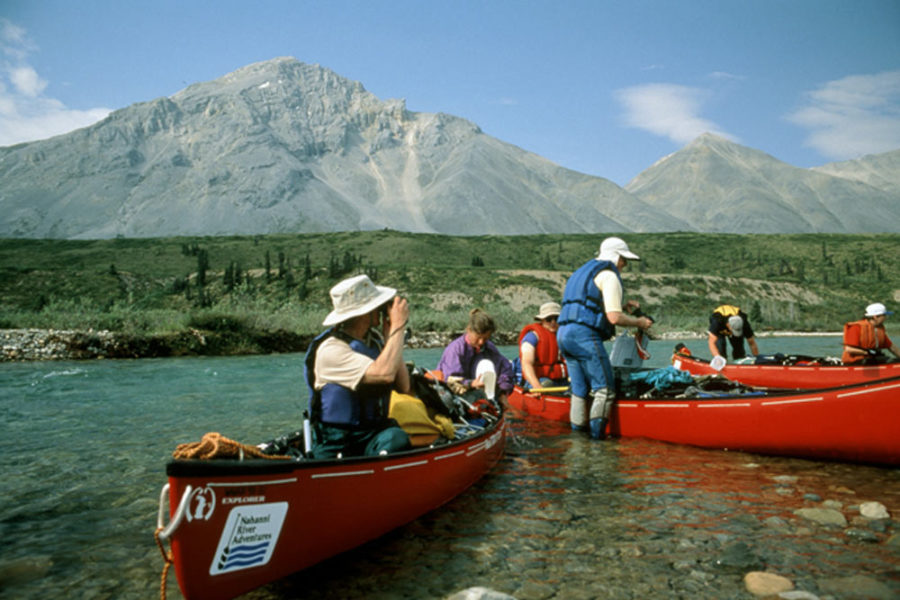 Several canoes on the Snake River in Yukon, Canada with mountains in the background.