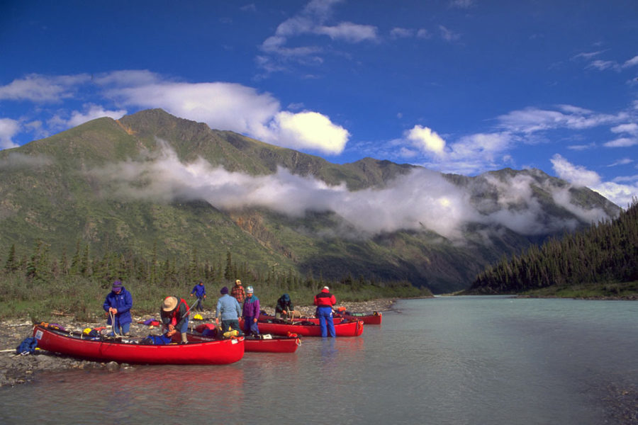 Several canoes on the shore of the Snake River in Yukon, Canada with mountains in the background.