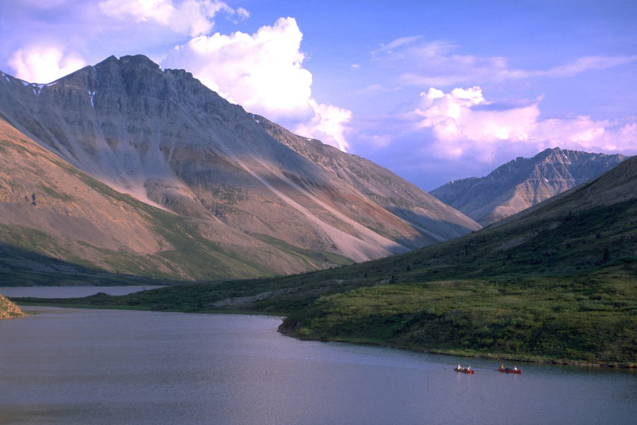 Two Canoes on the Snake River in Yukon, Canada. They appear dwarfed by massive mountains in the background.