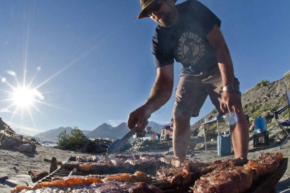 A guide from Canadian River Expeditions grilling dinner over open flames on our Alsek River Rafting Expedition.