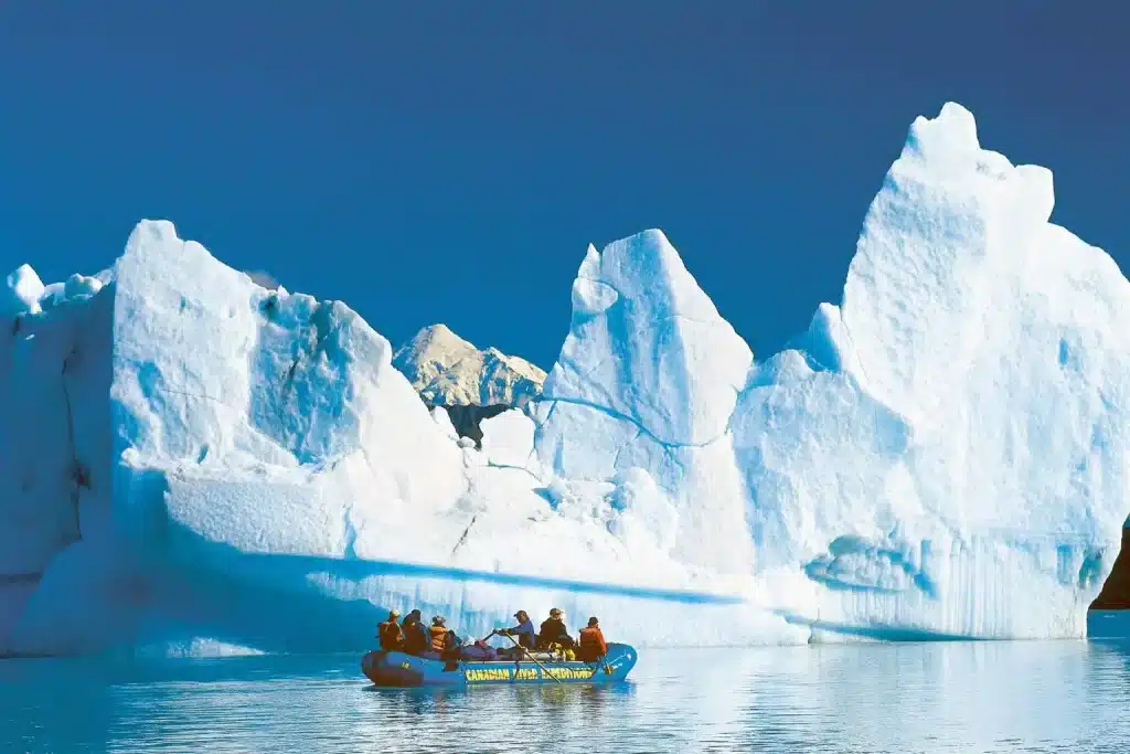 a group of people in a boat on water with icebergs in the background