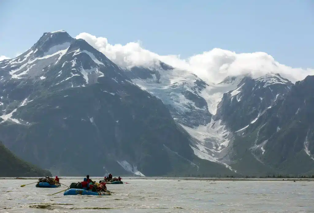 a group of people in rafts in a body of water with mountains in the background