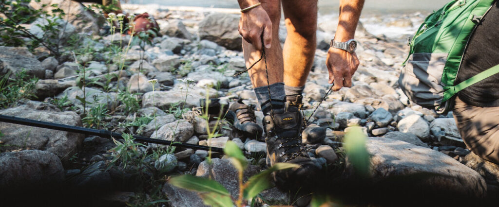 A hiker laces up their boots on the Nahanni River, NWT, Canada.