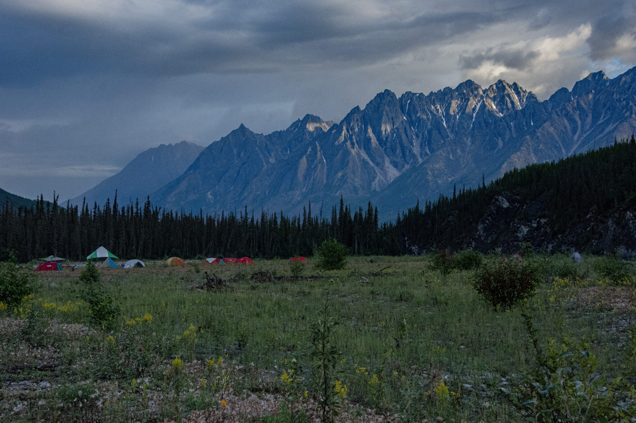 a campsite with tents in front of the ragged range mountains on the broken skull river, canada