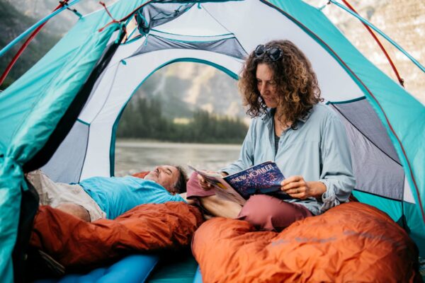 A couple reading and sleeping in a tent, Nahanni River, NWT, Canada.